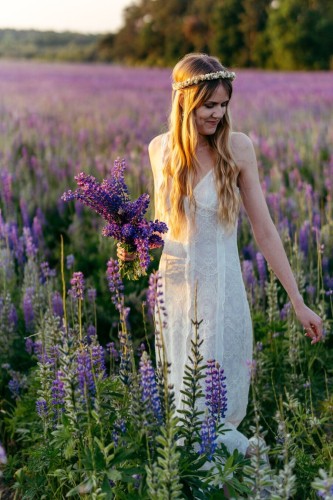 The photo of a standing woman in a lupine field.