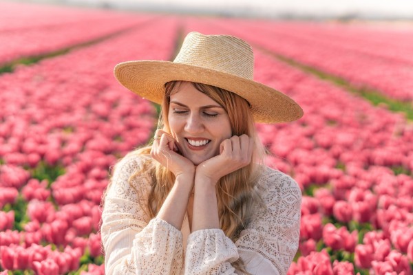 The photo of a smiling woman, with a field of pink tulips in the background.